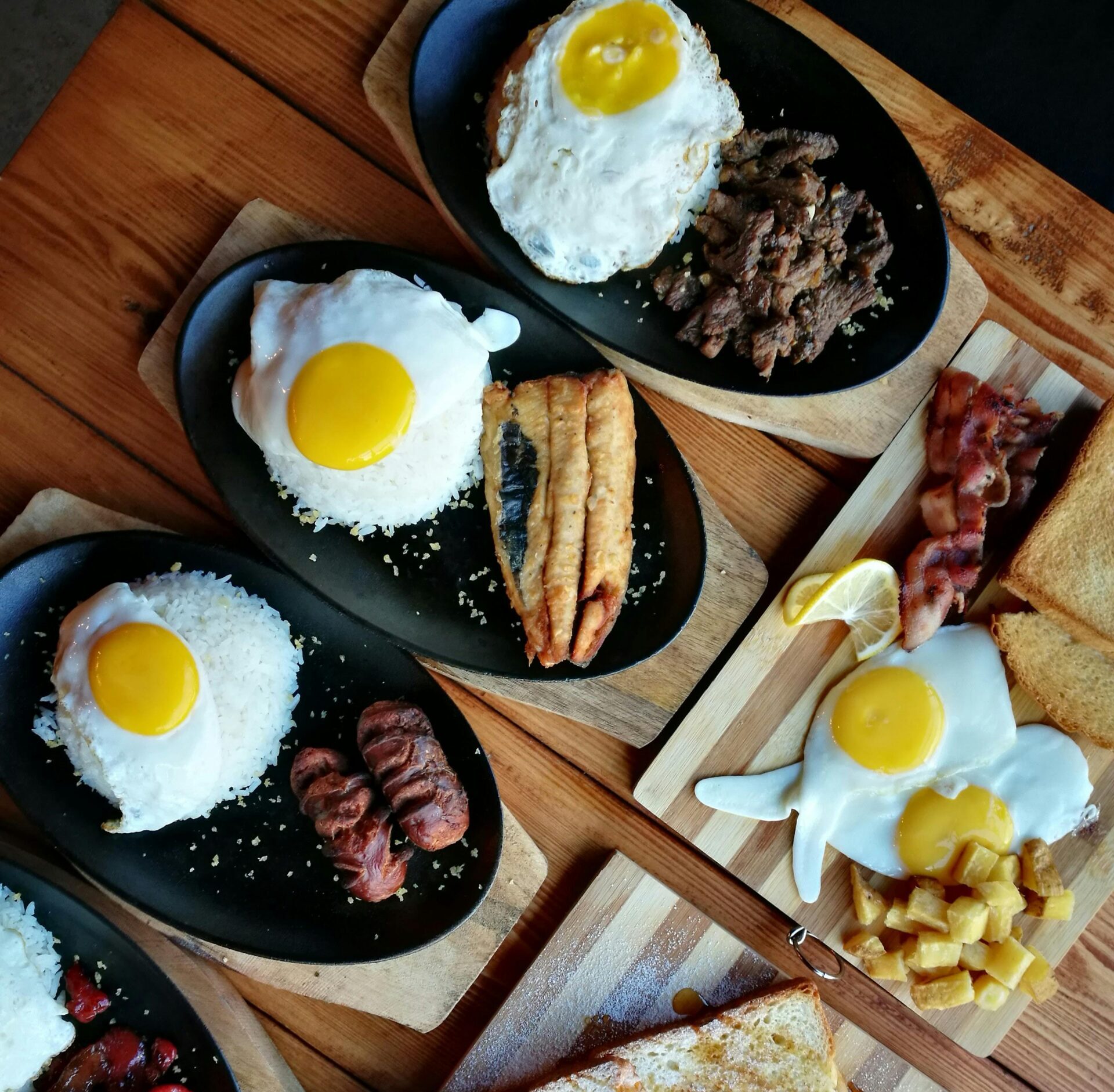 An appetizing breakfast spread featuring eggs, meats, toast, and rice on a wooden table.